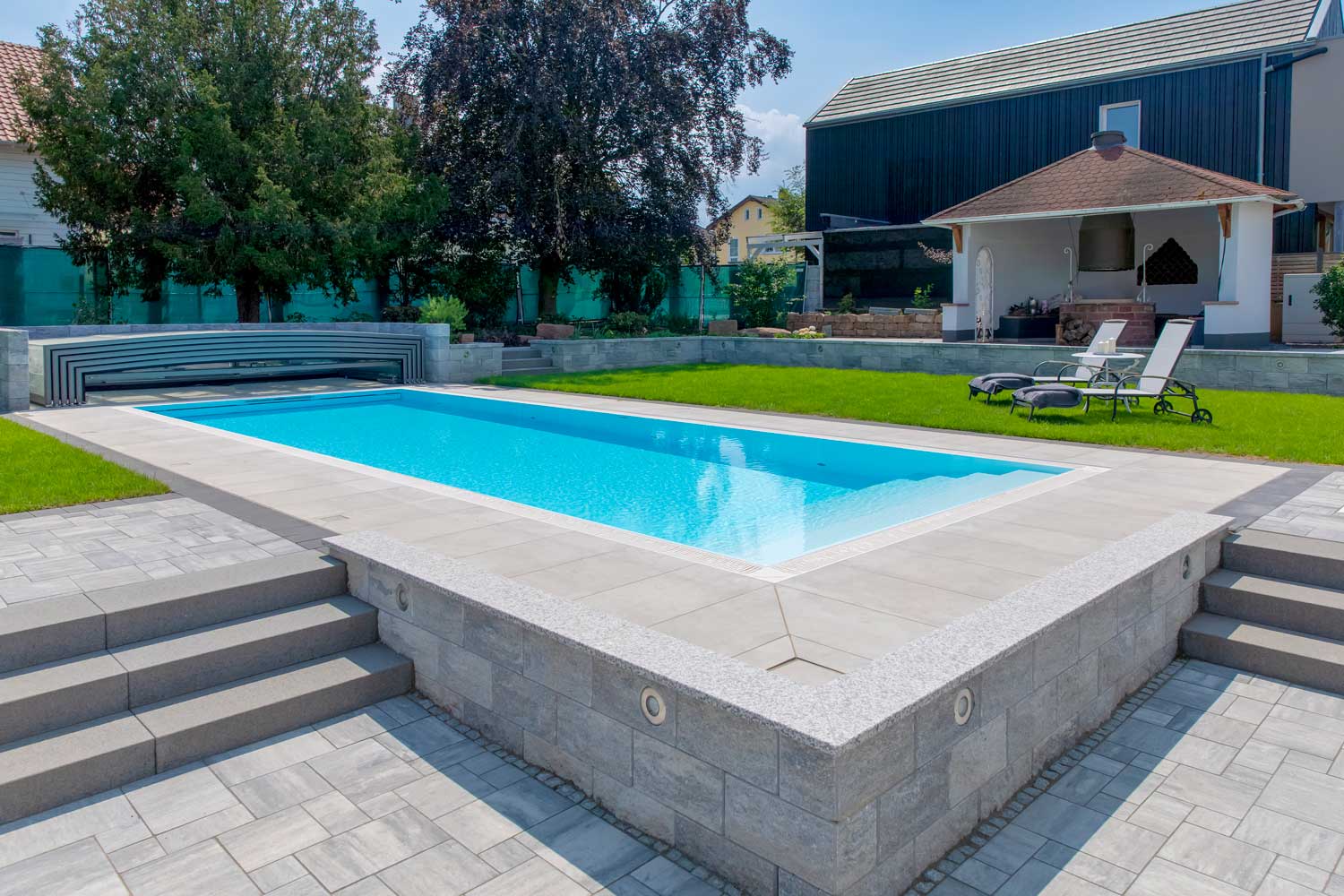 Ein leerer Pool in einem gepflegten Garten mit Liegestühlen und modernem Haus