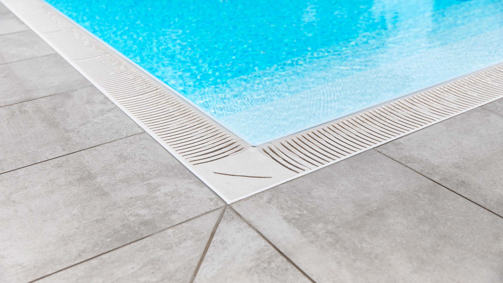 Ecke eines sauberen Pools mit hellem Wasser und grauen Fliesen am Beckenrand