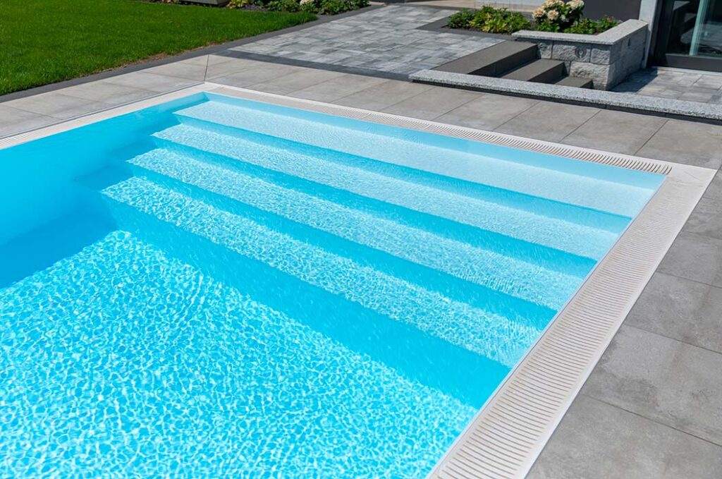 Ein leerer Pool mit klarem blauem Wasser, breiten weißen Stufen und grauen Fliesen