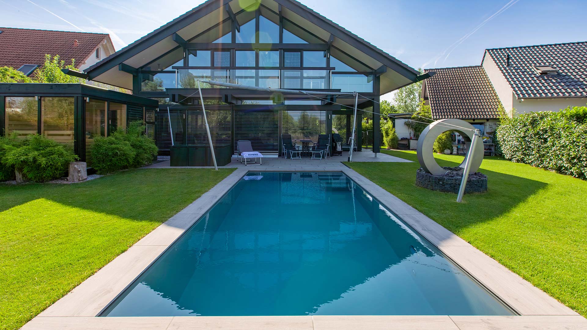 Modernes Haus mit großen Glasflächen, gepflegtem Garten und blauem Pool im Vordergrund