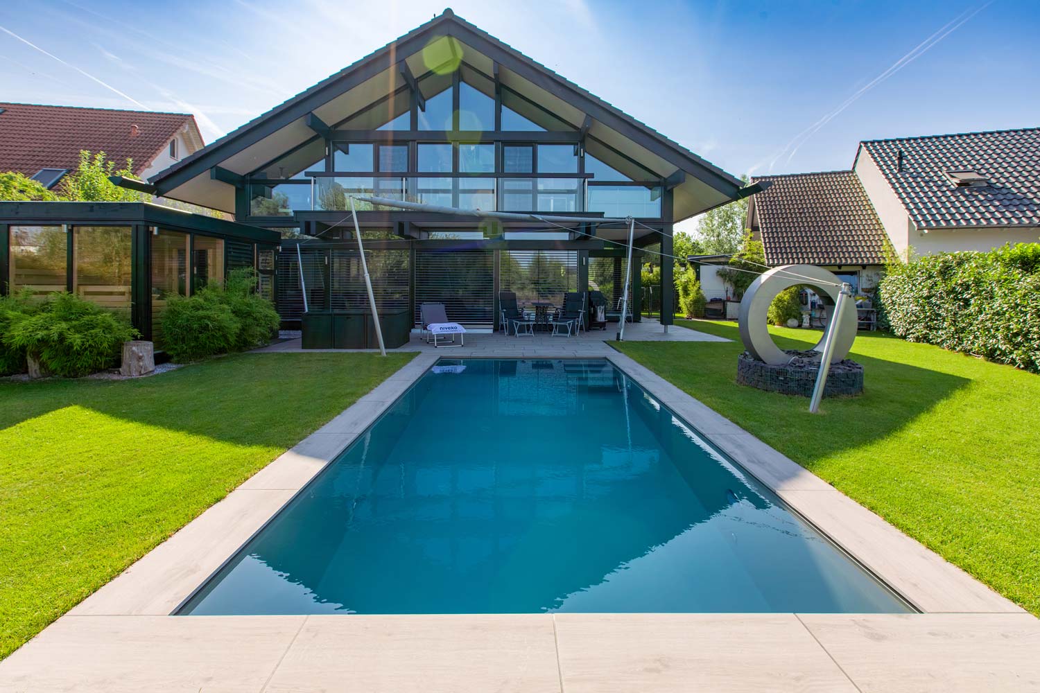 Modernes Haus mit viel Glas, gepflegtem Garten, Pool und großer Skulptur im Rasen