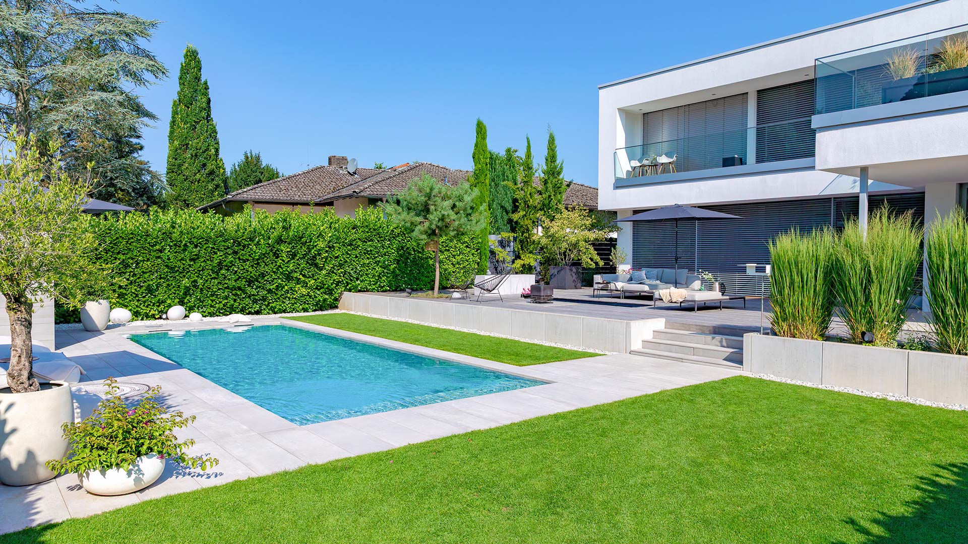 Modernes weißes Haus mit großem Pool im Garten, grüner Rasen und stilvolle Terrasse