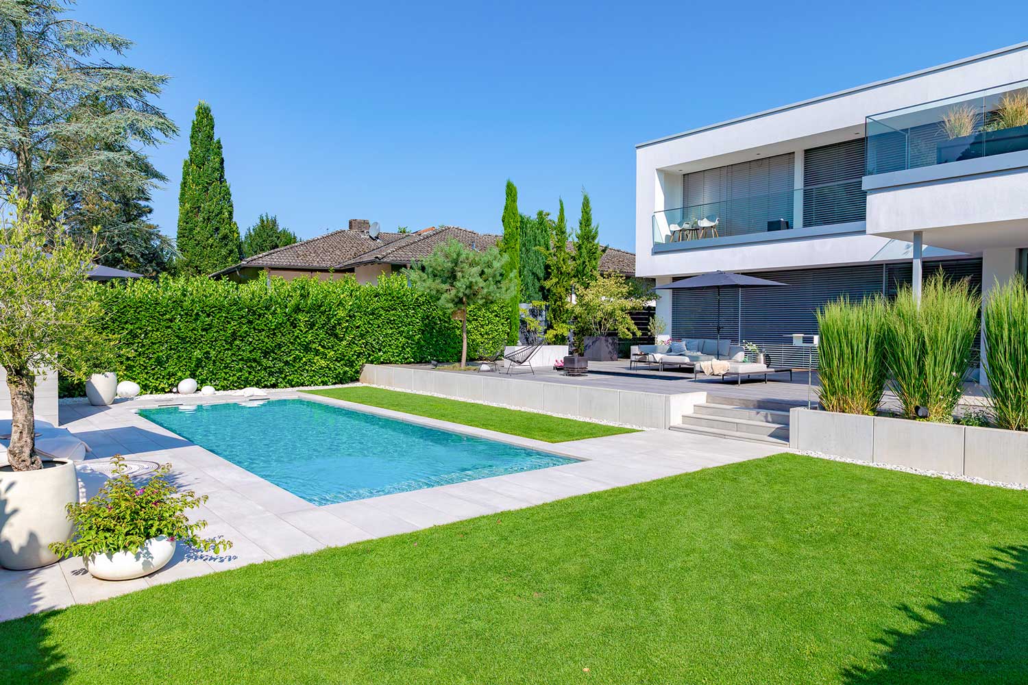 Moderner Garten mit grünem Rasen, rechteckigem Pool und weißem Haus im Hintergrund