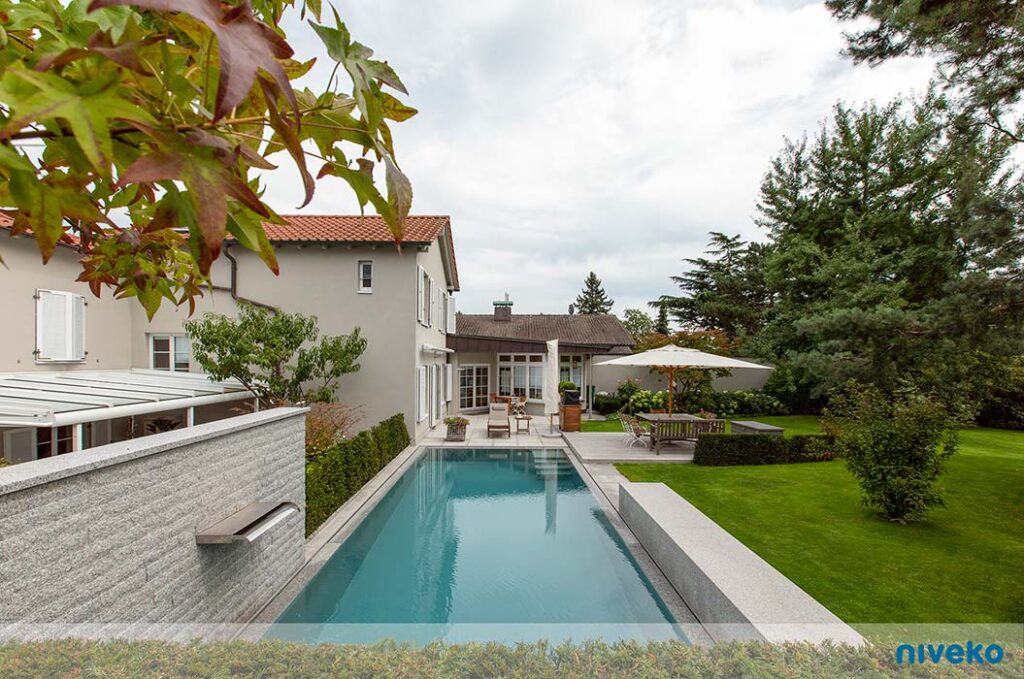 Modern weißes Haus mit langem Pool im gepflegten grünen Garten bei bewölktem Himmel