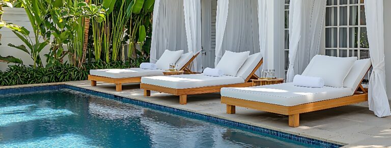 Drei luxuriöse weiße Liegen am Pool eines Resorts mit weißen Cabanas und üppiger tropischer Vegetation.