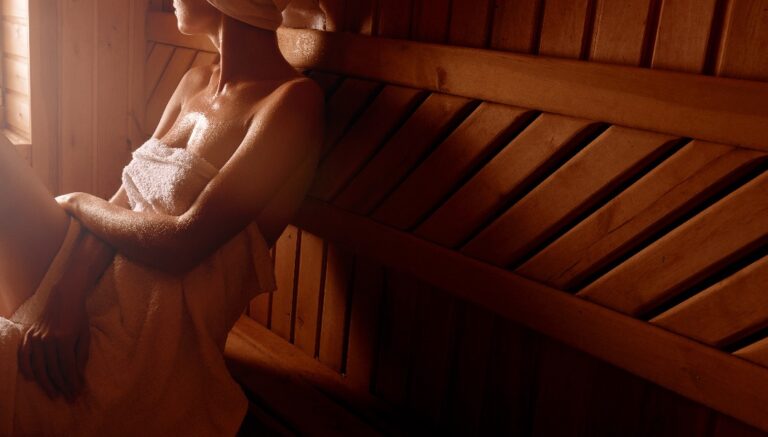 Ein Mädchen bei einer Wellnessbehandlung in einer traditionellen Sauna mit einem Hautbürsten und einem Waschlappen. Es entspannt sich, in ein weißes Handtuch gehüllt.