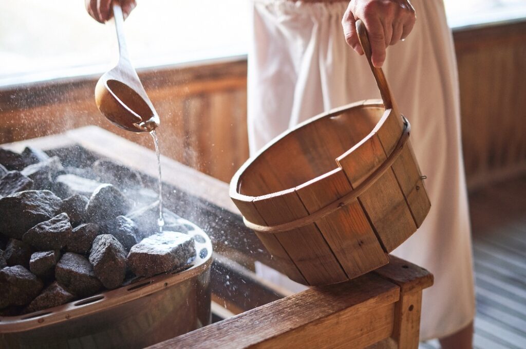 Ein Mann gießt Wasser auf heiße Steine in der Sauna.