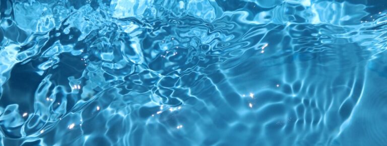Eine blaue, glitzernde Wasseroberfläche mit Sonnenreflexen im Schwimmbad als Hintergrund