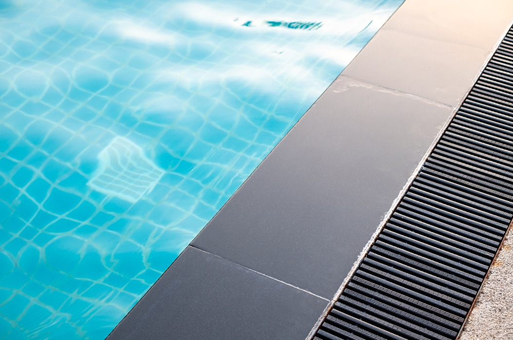 Eine schwarze Regenrinne wird neben dem Schwimmbecken, dem Entwässerungssystem, der Überlaufrinne, dem privaten Schwimmbecken und am Beckenrand installiert.