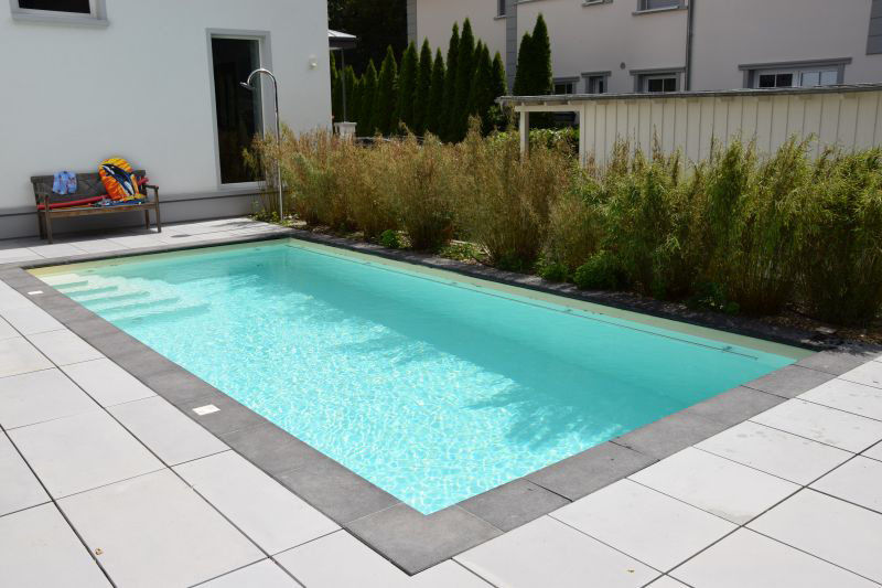 Ein heller moderner Pool mit klarem Wasser und grünen Pflanzen am Rand