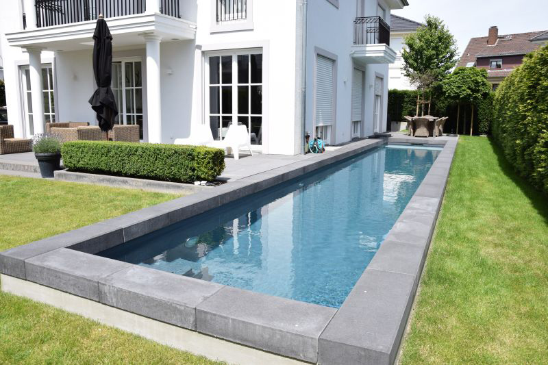 Eine moderne weiße Villa mit schmalem Pool im Garten und grüner Rasenfläche
