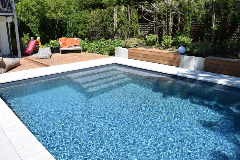 Ein leerer Pool im Garten mit klarem Wasser, Holzterrasse und bunter Rutsche