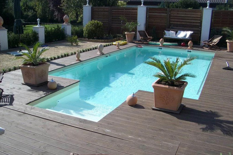 Ein moderner Pool mit klarem Wasser und Holzterrasse umgeben von Palmen in Töpfen