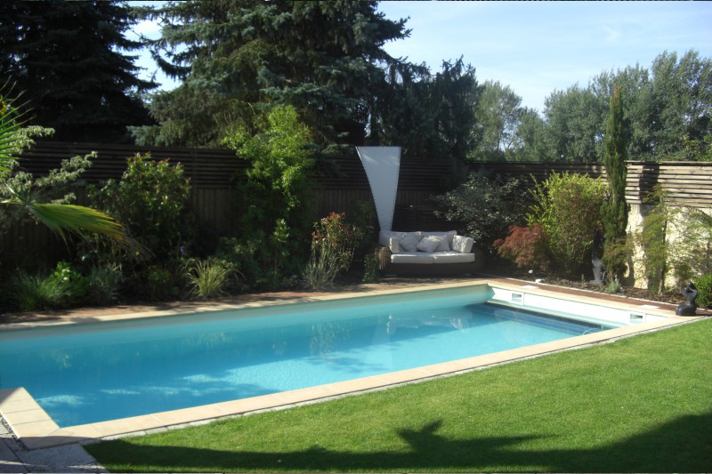 Ein Pool mit klarem Wasser liegt in einem grünen Garten mit vielen Pflanzen und einem Sofa