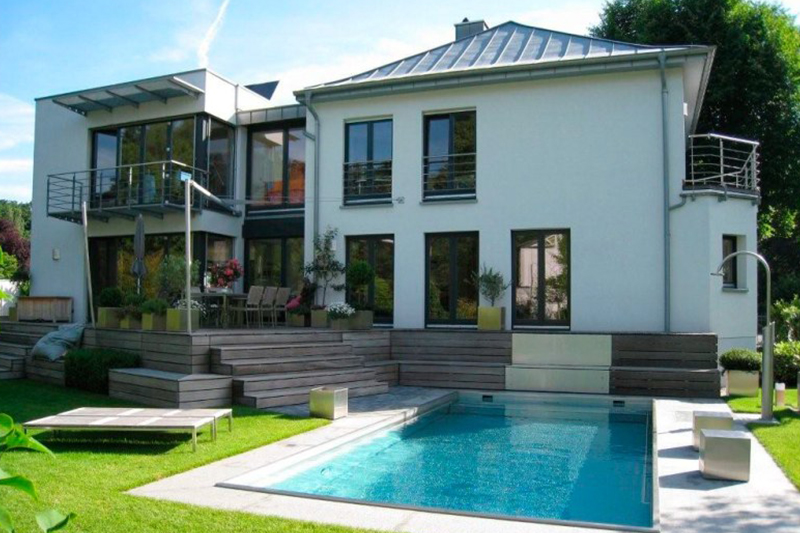 Modernes weißes Haus mit großen Fenstern, Holzelementen und blauem Pool im Garten