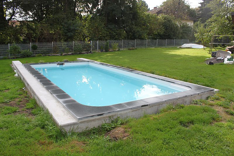 Ein rechteckiger Pool mit klarem Wasser liegt in einem grünen Garten