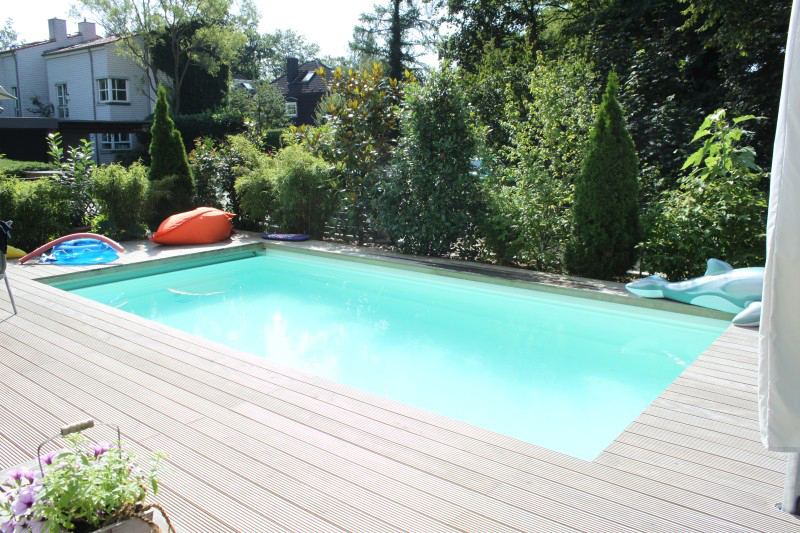Ein heller Gartenpool mit Holzterrasse und bunten Poolspielzeugen im Sonnenschein