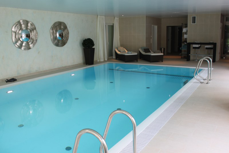 Heller Innenpool mit türkisfarbenem Wasser, modernen Liegen und dekorativer Wandkunst