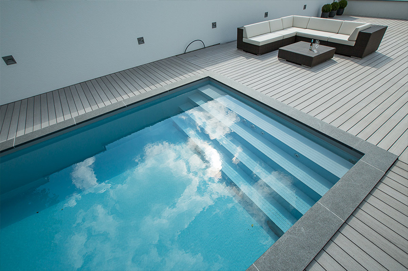 Ein moderner Pool mit klaren Stufen spiegelt die Wolken neben einer weißen Sitzecke