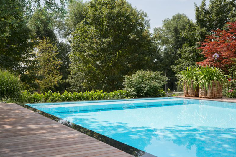 Ein leerer Swimmingpool mit klarem Wasser und Holzdeck, umgeben von grünen Bäumen
