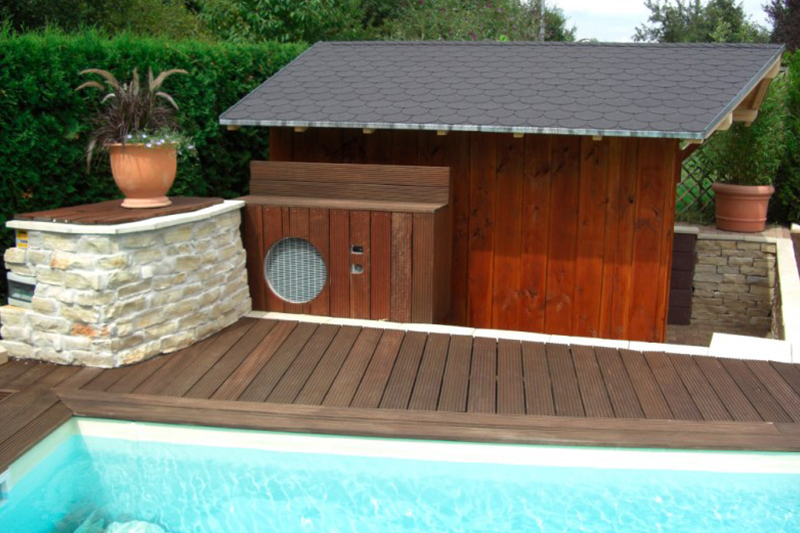 Ein Pool mit hellblauem Wasser, Holzterrasse und kleiner Holzhütte mit Ventilator
