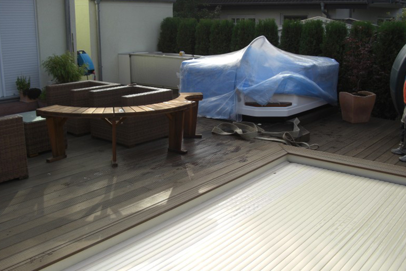 Ein Whirlpool mit blauer Folie abgedeckt steht auf einer Terrasse mit Rattanmöbeln