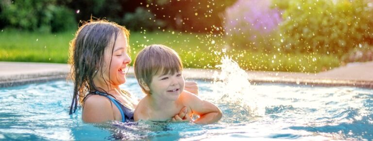Glückliche Geschwister spielen im Swimmingpool im Garten. Eine Schwester im Vorjugendalter bringt ihrem kleinen Bruder das Schwimmen bei. Lebensstil und Freizeitbeschäftigung in den Sommerferien.