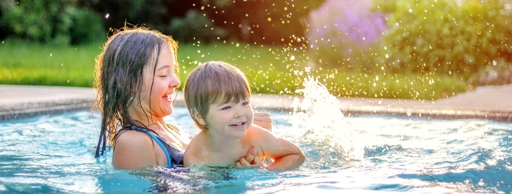 Glückliche Geschwister spielen im Swimmingpool im Garten. Eine Schwester im Vorjugendalter bringt ihrem kleinen Bruder das Schwimmen bei. Lebensstil und Freizeitbeschäftigung in den Sommerferien.