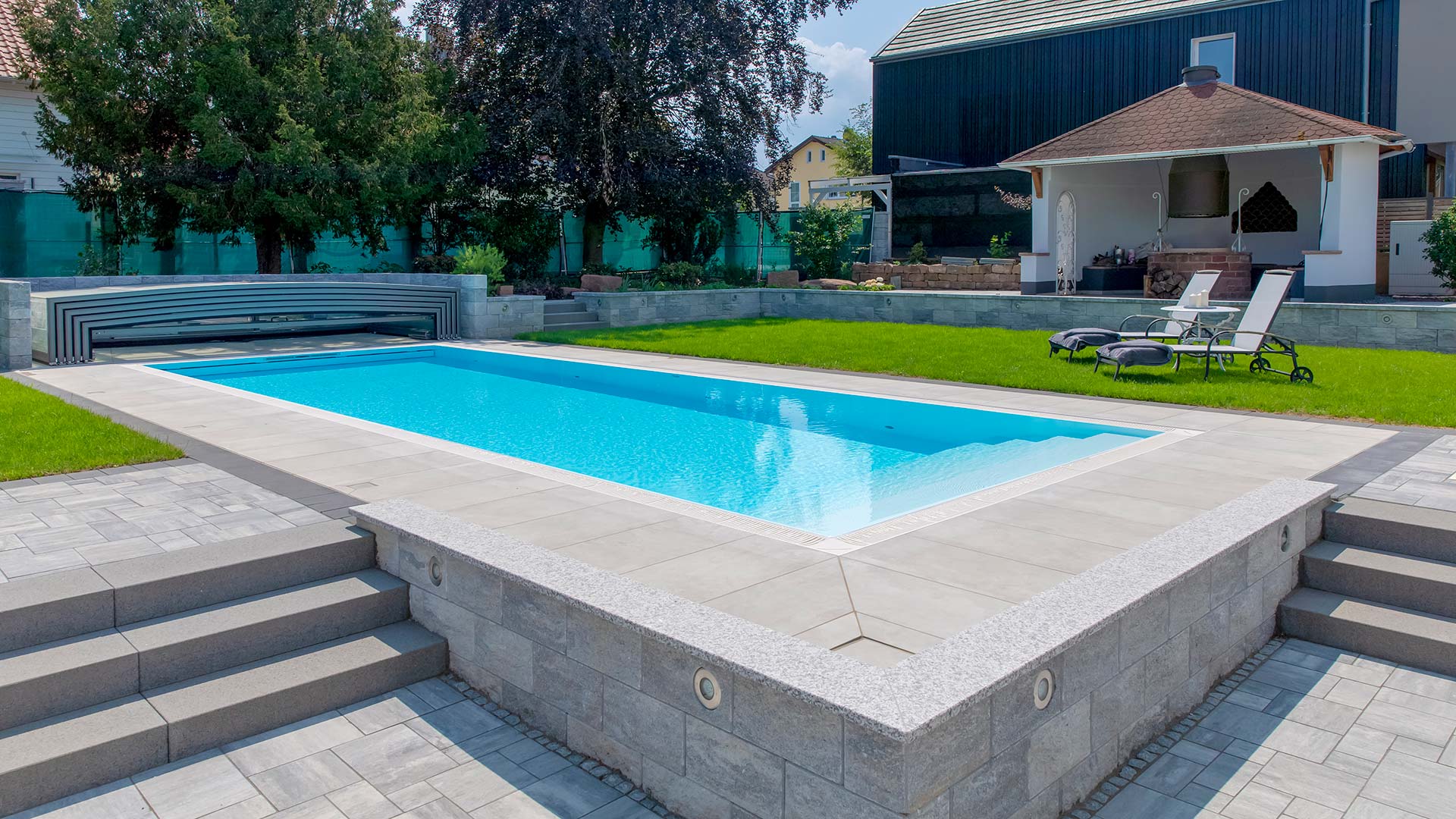 Ein moderner Pool mit hellem Randstein, klarem Wasser und grüner Rasenfläche