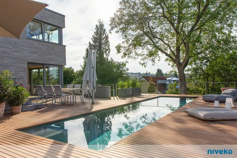 Moderner Poolbereich auf Holzterrasse neben einem Haus mit Gartenmöbeln und Pflanzen