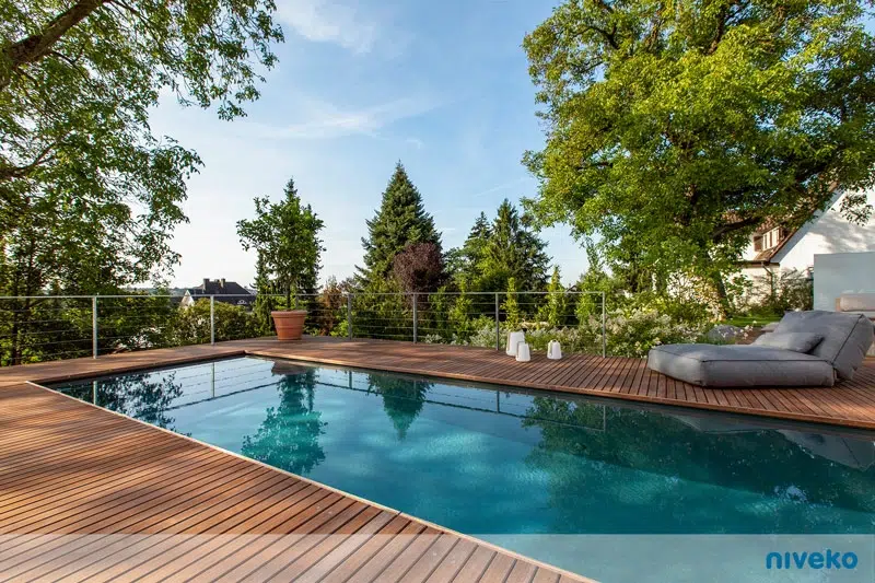 Ein moderner Gartenpool mit Holzterrasse und gemütlicher grauer Liege bei Sonnenschein