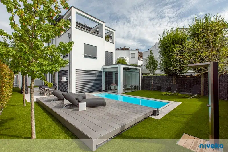 Modernes weißes Haus mit Pool, großen Fenstern und gepflegtem grünen Garten
