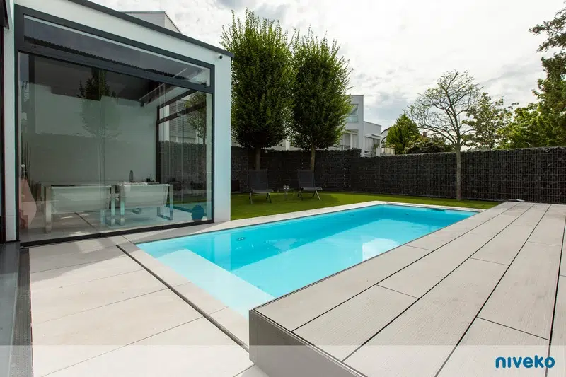 Ein moderner Garten mit Pool, hellen Fliesen und eleganter Glasfassade