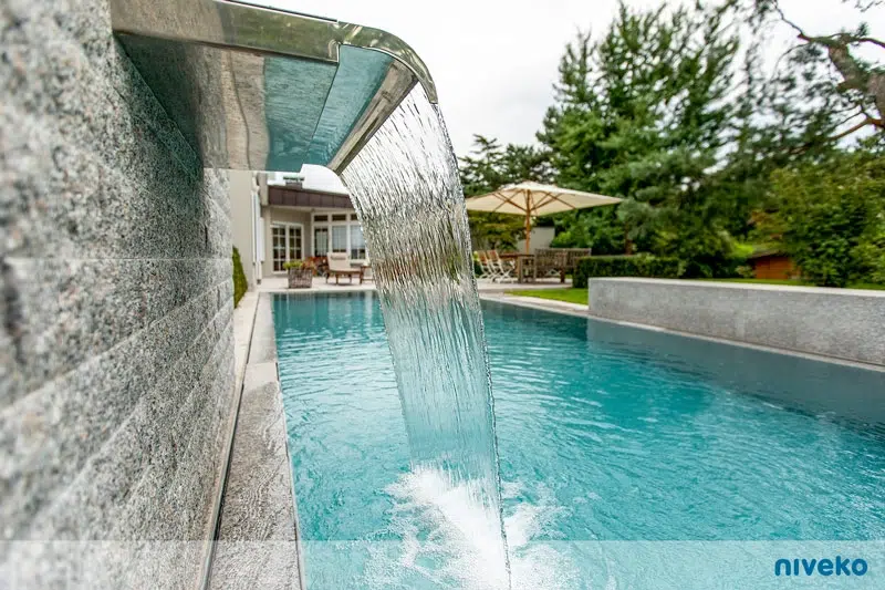 Ein moderner Swimmingpool mit Wasserfall und klarem türkisblauem Wasser im Garten