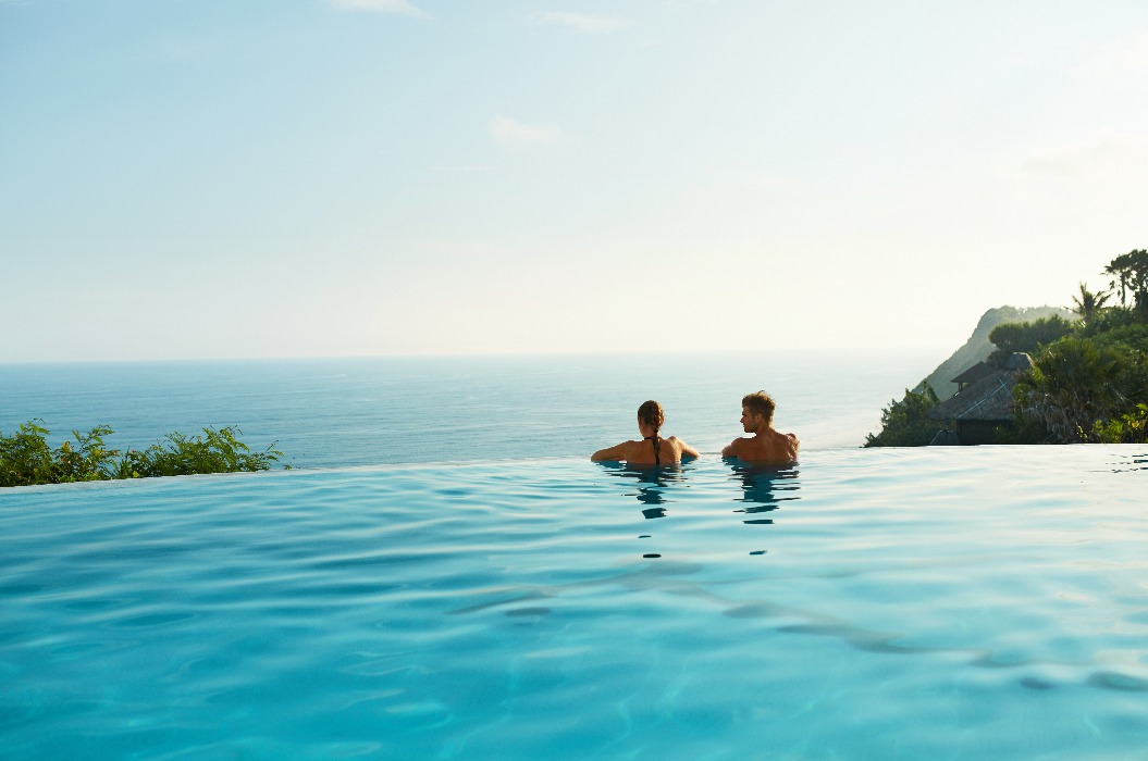 Romantischer Urlaub für ein verliebtes Paar. Glückliche Menschen, die sich im Wasser eines Infinity-Pools entspannen und den wunderschönen Meerblick genießen. Ein Mann und eine Frau gemeinsam auf einer Sommerreise in ein Luxusresort. Sommerliche Entspannung