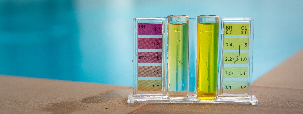 Überprüfung der Wasserqualität eines Schwimmbeckens mithilfe eines chemischen Testkits zum Vergleich des pH-Werts und der Chlorkonzentration; Foto mit unscharfem Hintergrund, auf dem die Wasseroberfläche deutlich blau zu sehen ist.
