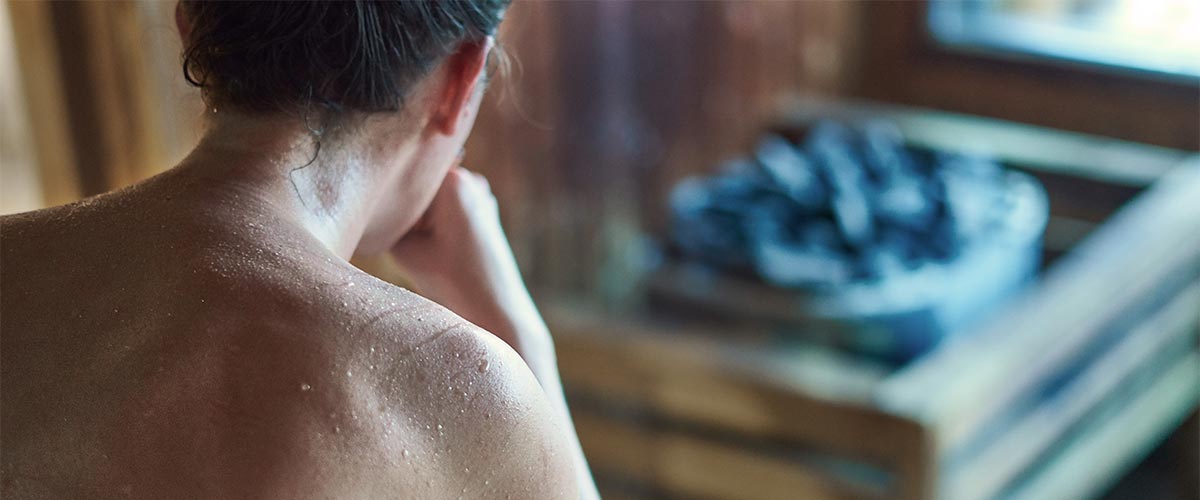 Frau sitzt schwitzend in Sauna.