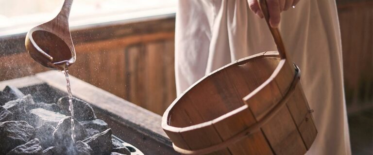 Man pouring water into hot stone in sauna room.