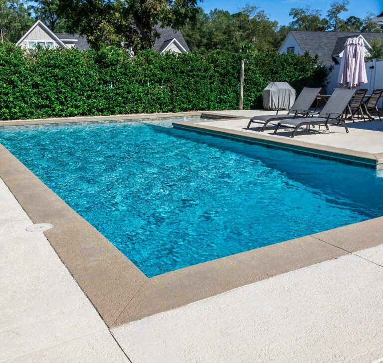 Rechteckiger neuer Swimmingpool mit sandfarbenem Betonrand im eingezäunten Garten eines Neubaus