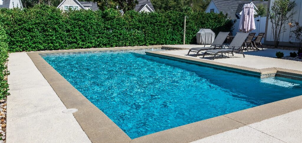 Rechteckiger neuer Swimmingpool mit sandfarbenem Betonrand im eingezäunten Garten eines Neubaus