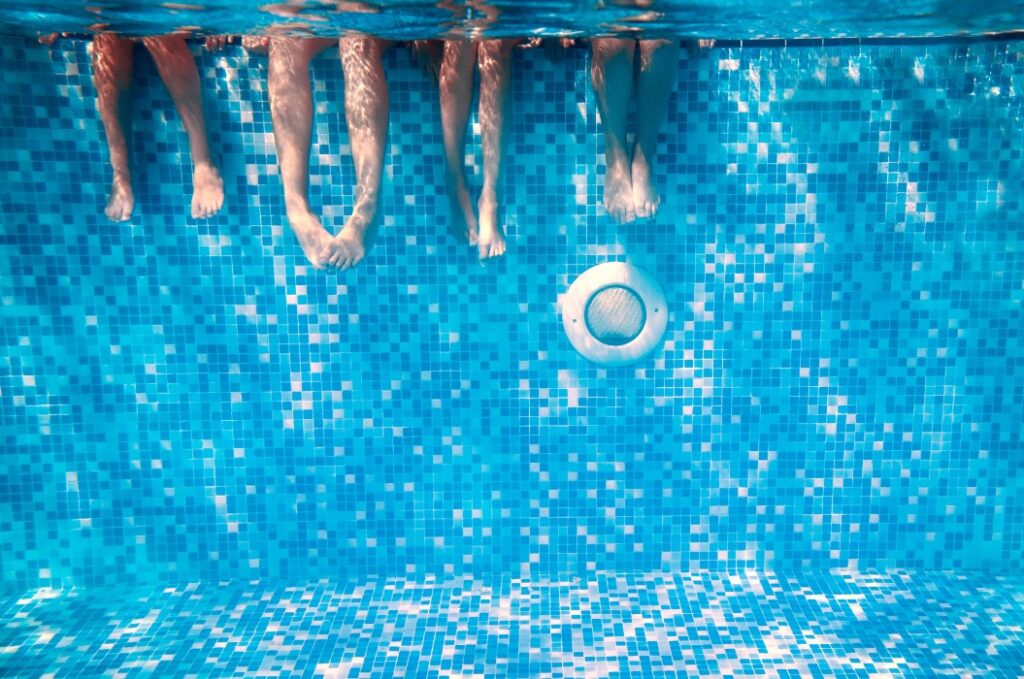 Beine von Kindern und Erwachsenen unter Wasser im Schwimmbad